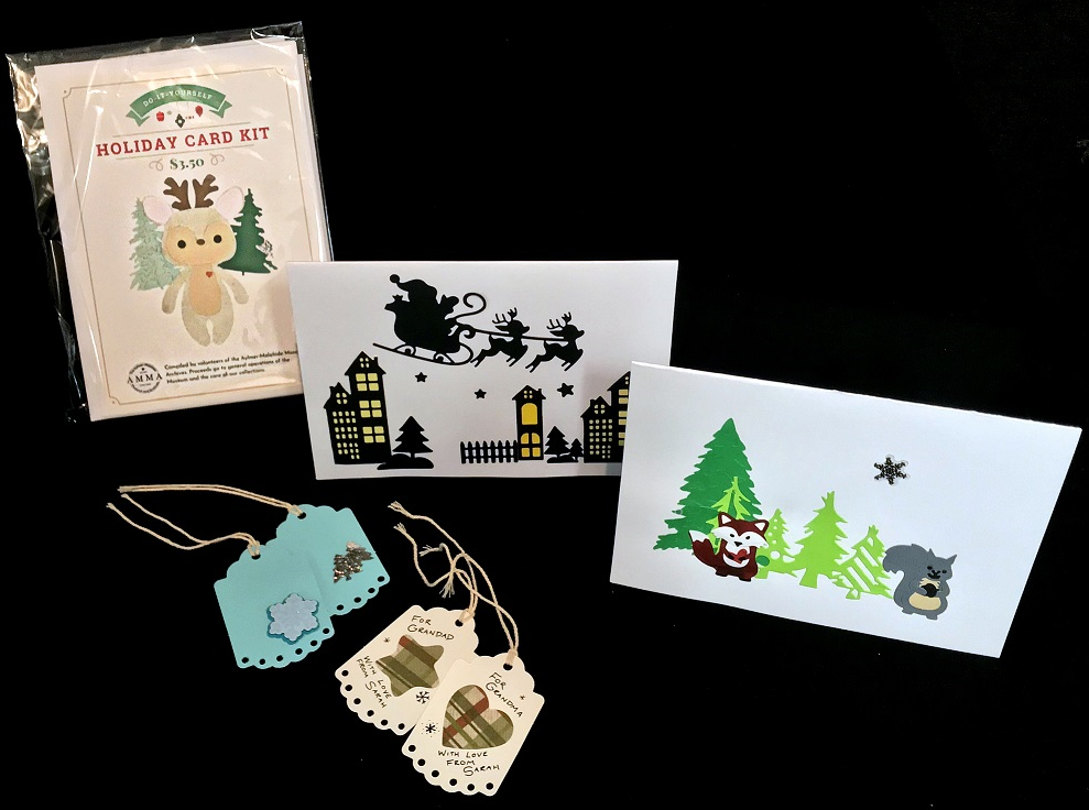 Pictured: the Holiday Card Kit package, a card decorated with little woodland animals in front of a forested scene, a card decorated with the silhouette of a small town, Santa Claus flying overhead in a sleigh, two blue gift tags decorated with snowflakes and trees, and two white gift tags decorated with a plaid star and a plaid heart.