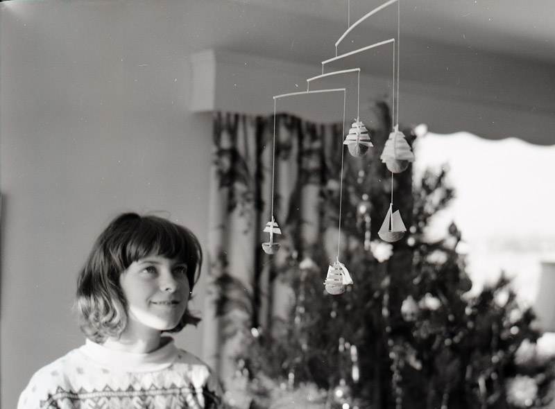 Black and white image of a young girl looking up at a mobile.