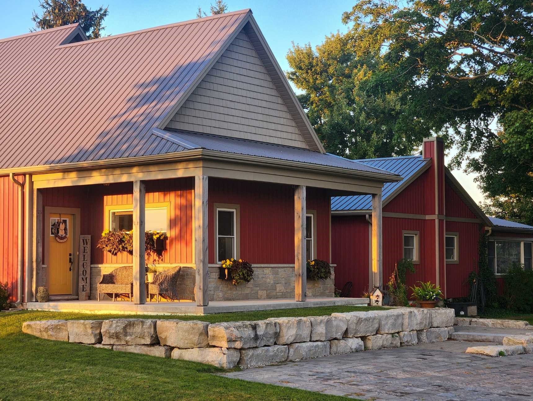 13654 Putnam Road. Two ranch-style buildings with red siding and grey roofing, the foremost of which has a wraparound porch. The door is painted yellow, and a sign that reads 