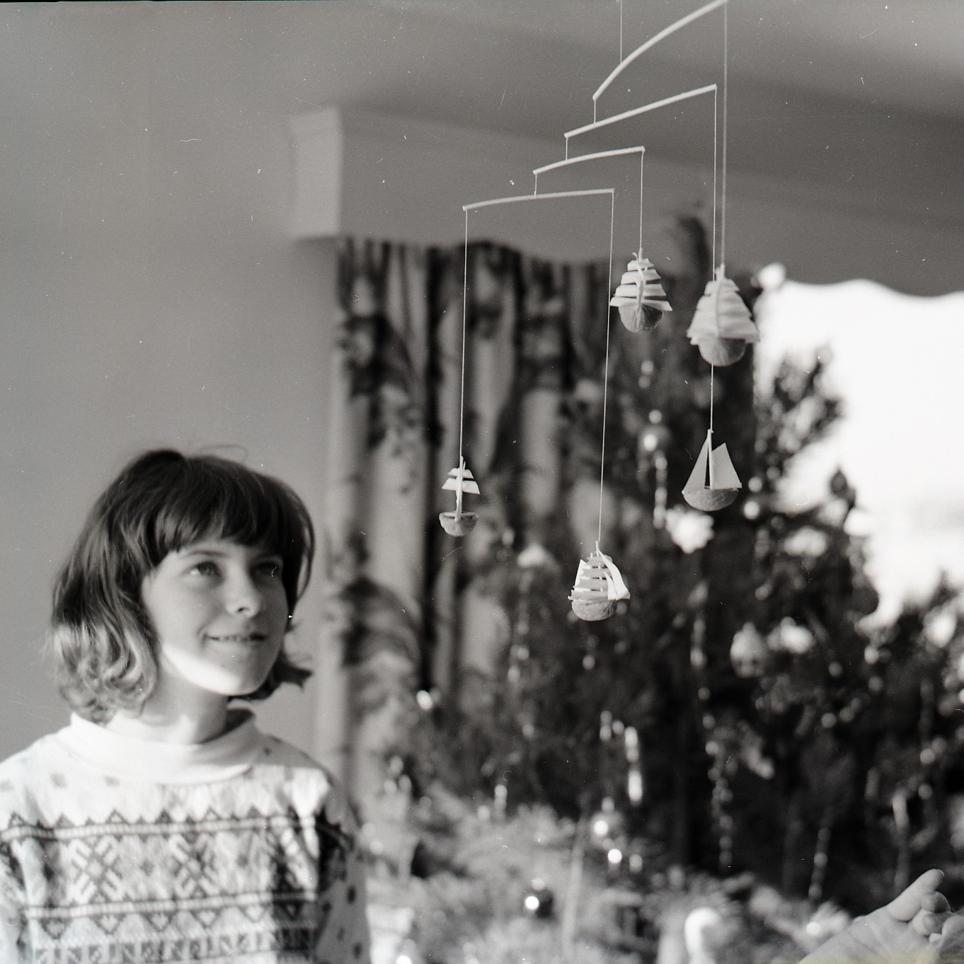Image of a young woman looking upward at a toy mobile, with a Christmas tree in the background